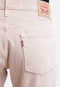 Jeans Levi's 501 CT en denim beige suave. Cuenta con un bolsillo trasero con etiqueta de cuero marrón, una pestaña roja en el costado y la típica costura curva.