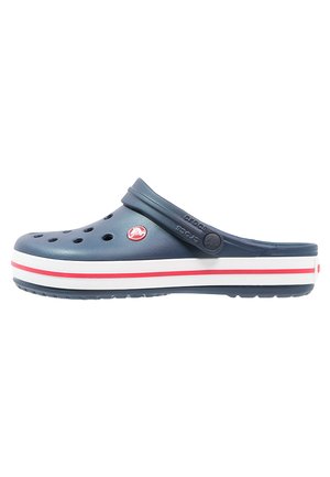 Sabots en caoutchouc bleu avec des trous de ventilation, semelle blanche ornée de rayures rouges et une sangle arrière pour un ajustement sécurisé. Loge Crocs visible sur le côté.