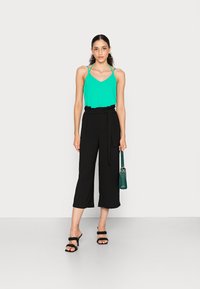 Top sem mangas verde menta com alças finas, combinado com culotes pretos de cintura alta e sandálias pretas de salto. Pequena bolsa verde.