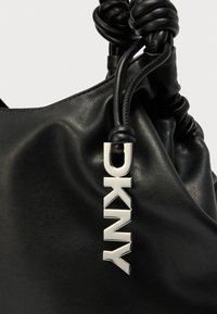 Mustast nahast käekott pehme tekstuuri, voltitud disaini ja hõbedase Dkny logoga. Omab sõlmitud sangasid, mis lisavad detaili.