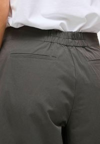 Pilkos spalvos kelnės su elastinga liemens juosta, dviem kišenėmis gale, su lygiu, matinio paviršiaus audiniu ir siauru kirpimu. Juosmuo su rautiėmis patogumui.