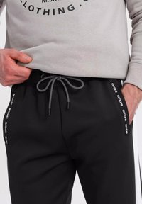 Zwarte sweatpants van zachte stof, met een elastische tailleband met een trekkoord en zijaccenten met "ombre"-tekst in het wit.