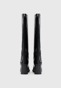 Botas negras hasta la rodilla hechas de un material sintético brillante, con una cremallera trasera y un tacón cuadrado, de textura suave y diseño minimalista.