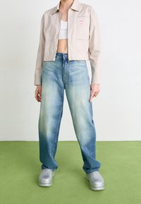 Cropped beige striped jacket, light blue faded jeans, and silver clogs with a chunky sole. Notable pink patch on the jacket.