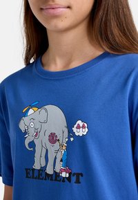Blå bomulds T-shirt med et grafisk design af en elefant med en propellerhat og en person, der maler den, med ordet "ELEMENT" nedenunder.