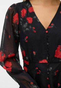 Crna cvjetna haljina s crvenim ružama, dugim prozirnim rukavima, dubokim V-izrezom i pet dugmadi sprijeda. Lagan materijal s mekanom teksturom.