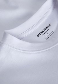 Bijela pamučna majica s okruglim izrezom, s glatkom teksturom i vidljivim šavovima; oznaka glasi "JACK & JONES ESSENTIALS."
