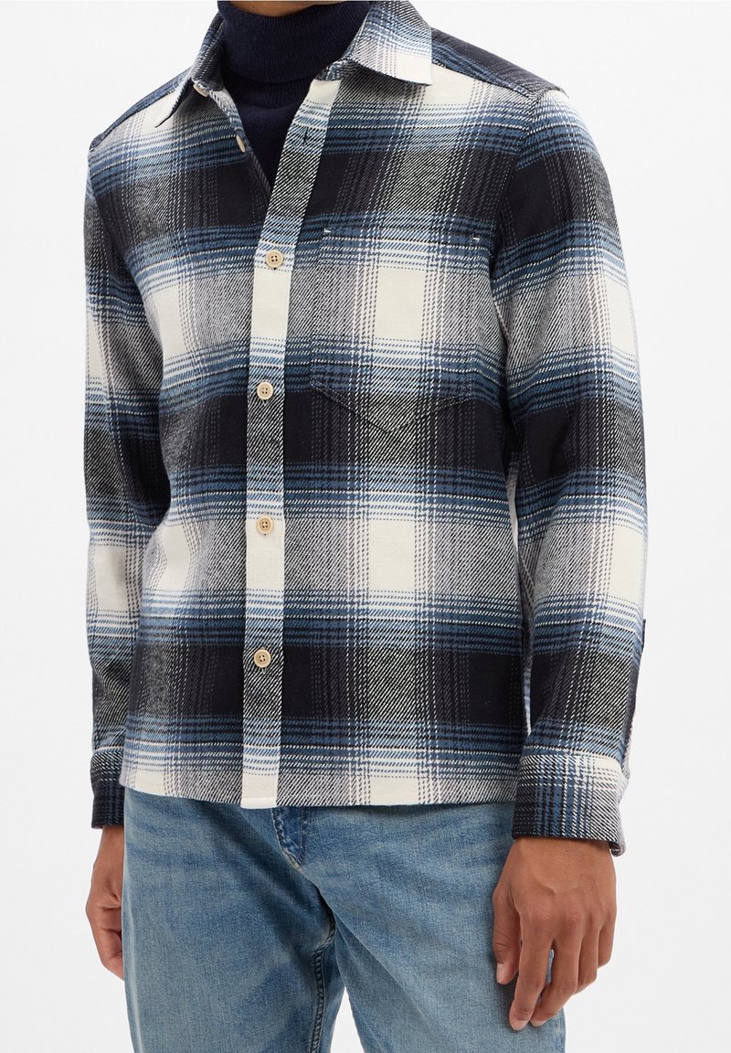 Plaid shirt in blues, black, and white; features buttons and chest pocket; made of textured fabric; long sleeves and collared design.