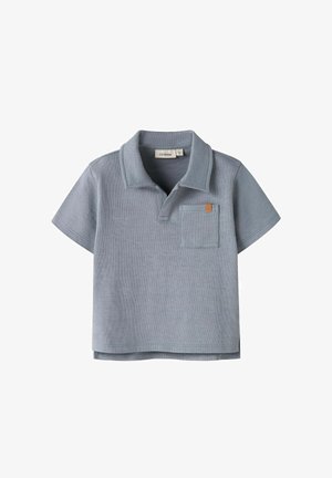 Polo de punto de manga corta en azul claro con cuello abierto y pequeño bolsillo en el pecho con una etiqueta marrón.