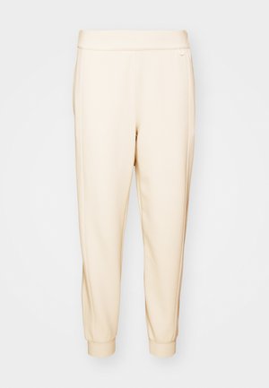Pantalones de chándal beige, ajustados en la parte inferior, hechos de una tela suave, con una cintura elástica y puños ajustados en los tobillos. Diseño minimalista, sin patrones visibles.
