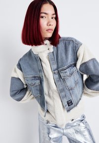 Denimjakke med cremet shearling-foring og ærmer, har frontlommer, en cropped silhuet og et mærke på den nederste kant.