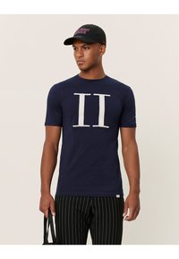 Camiseta de corte corto en navy con gráfico texturizado blanco "II" en el frente, combinada con pantalones a rayas negros y una gorra negra.