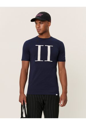 Camiseta de corte corto en navy con gráfico texturizado blanco "II" en el frente, combinada con pantalones a rayas negros y una gorra negra.