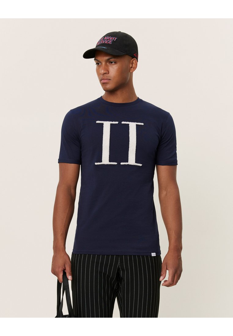Camiseta de corte corto en navy con gráfico texturizado blanco "II" en el frente, combinada con pantalones a rayas negros y una gorra negra.