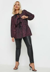 Mustikkamustalla ja burgundinpunaisella leopardikuosisella paitapuserolla, jossa on pitkät hihat, nauhavyö tiedäntä kaulassa ja peplum-helma, yhdistettynä mustiin tekonahkahousuihin ja korsettikorkoihin.