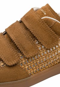 Brown suede sneaker with three velcro straps and woven light brown accents. Textured surface and rubber sole. Simple, casual design.
