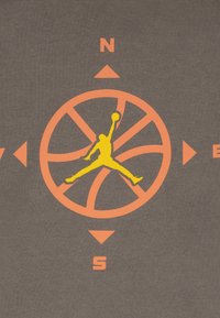 Γκρι ύφασμα με μεγάλο πορτοκαλί σχέδιο πυξίδας με σημάδια κατεύθυνσης και κίτρινη εικόνα περιγράμματος παίκτη μπάσκετ που κάνει άλμα για σουτ.