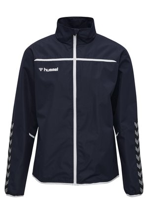 Marinblå vindjacka med hög krage, vit dragkedja, vita ränder över bröstet och chevrondetaljer på ärmarna.