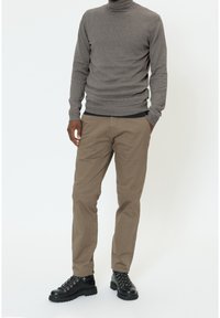 Pull à col roulé gris associé à un pantalon chino beige et des bottes noires à lacets. La tenue présente une coupe ajustée et un tissu texturé.