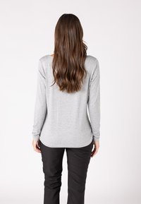 Graues Langarmshirt aus weichem Stoff, runder Ausschnitt und abgerundeter Saum. Kombiniert mit schwarzen Hosen, von hinten betrachtet.