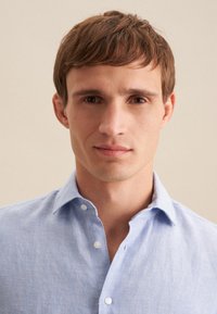 Jasnoniebieska koszula z guzikami o miękkiej fakturze, z klasycznym kołnierzykiem i delikatnym splotem materiału, wyeksponowana na neutralnym tle.