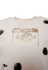 Jasnoróżowy T-shirt z nadrukiem złotego vintage aparatu, ozdobiony czarnymi kropeczkami rozmieszczonymi na materiałach.