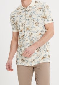 Poloko s krátkým rukávem s květinovým vzorem v krémové barvě, s světle modrými a hnědými květy, klasickým límečkem a knoflíkovou légou. Měkká textura.