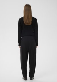 Črn pleten pulover in ohlapne črne hlače, pogled od zadaj, gladka tekstura s popolnoma ravnimi hlačnicami, minimalistična zasnova, brez vidnih vzorcev.