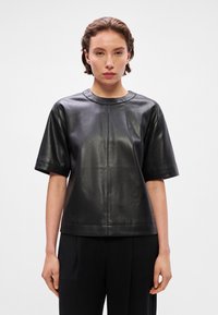 Top curto de manga curta em couro preto com decote redondo, apresentando uma textura suave e um design minimalista; sem padrões ou detalhes visíveis.