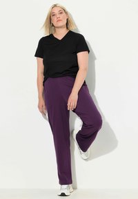 T-shirt noir à col en V associé à un pantalon avec taille élastique violet, tous deux en tissu lisse. Le modèle porte des baskets blanches.