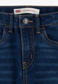 Jeans Levi's 710 Super Skinny en denim azul oscuro. Cuenta con cierre de botón, costuras marrones y diseño clásico de cinco bolsillos.