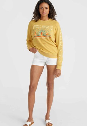 Geel sweatshirt met grafische print, lange mouwen, geribbelde manchetten, gecombineerd met witte shorts. Model met open-toe sandalen, staand op een effen achtergrond.