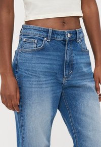 Jeans de cintura alta em denim azul escuro com um design clássico de cinco bolsos, costura visível e um acabamento desbotado para um efeito gasto.