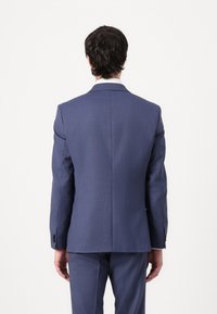 Chaqueta de traje azul vista desde la parte posterior, con un diseño a medida, forma estructurada y una textura sutil. Los botones están en los puños.
