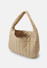 Beige quiltet håndtaske med et buet håndtag, der har en lynlåslukning og en blød stoftekstur. Vinklet form med en enkelt udvendig lomme.