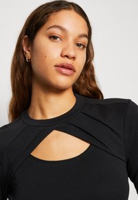 Maglietta nera a maniche lunghe con dettaglio a taglio al petto, realizzata in tessuto morbido e elasticizzato, con scollatura rotonda e pieghe sottili.