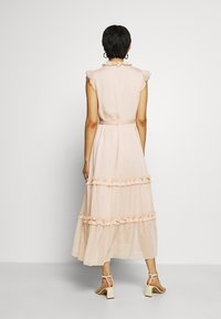 Vestido largo rosa claro hecho de un tejido fluido. Presenta acentos con volantes en los hombros y el dobladillo, con una cintura entallada y detalle de cinturón.