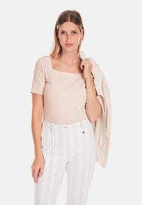 Beige fitted top with short sleeves and square neckline, paired with white patterned high-waisted pants featuring a zigzag design.