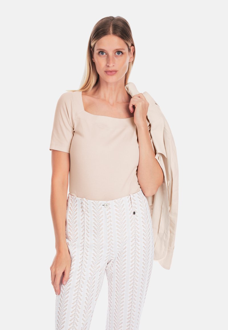 Beige fitted top with short sleeves and square neckline, paired with white patterned high-waisted pants featuring a zigzag design.