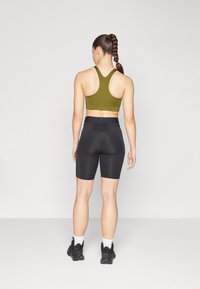 Zöld sportmelltartó széles pántokkal, fekete, magas derekú kerékpáros shortssal párosítva. Az öltözet szoros illeszkedést és sima textúrát jellemző.