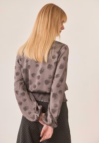 Blusa de satén gris con patrones de hojas negras, con mangas abullonadas y una cintura fruncida, combinada con una falda negra texturizada.