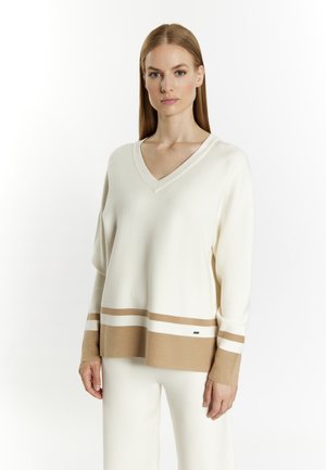 V-Ausschnitt, langärmeliger Pullover in Creme mit einem beige-weißen gestreiften Saum. Weicher Stoff, lockere Passform, minimales Branding-Detail am Saum.