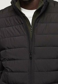 Giacca nera imbottita con zip frontale, caratterizzata da un design a cuciture verticali, colletto alto e rivestimento interno verde a contrasto.