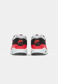 Adidași Nike Air în culorile negru, alb și roșu strălucitor, cu plasă texturată și piele, având o guleră căptușită și un branding proeminent pe călcâi.