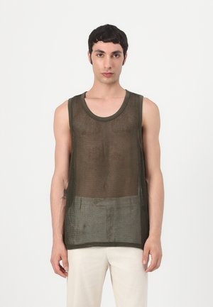 Mannelijk model draagt een olijfgroene mouwloze mesh tanktop en lichtbeige broek, staand tegen een effen witte achtergrond.