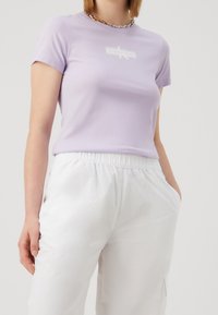 Lila kortemouwen t-shirt van zacht stof, met een witte logo-detail op de borst en gecombineerd met witte broek met elastische taille.