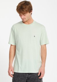 Lys grøn kortærmet t-shirt lavet af blødt materiale. Har et lille lilla logo på venstre bryst. Enkel, afslappet pasform.