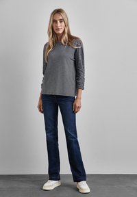 Graues Langarmoberteil mit horizontalen Streifen, kombiniert mit dunkelblauen Schlagjeans und weißen Sneakers, vor einem neutralen Hintergrund.