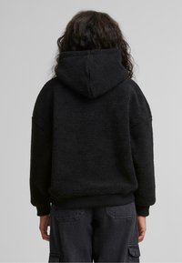 Felpa nera in pile con superficie testurizzata, vestibilità over-size e cappuccio. Polsini e orlo a coste, abbinata a pantaloni cargo scuri.