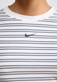 Camiseta blanca de algodón con rayas horizontales en azul marino. Presenta un pequeño logo negro de Nike en el pecho y un clásico escote redondo.